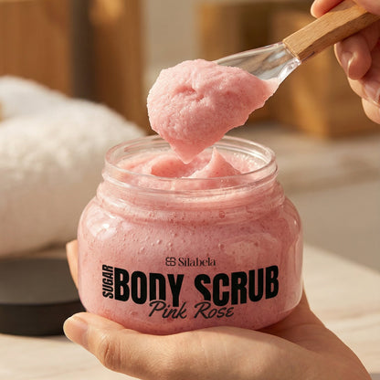 Pink body scrub being scooped with a wooden spoon from a jar labeled 'Body Scrub Pink Rose'.